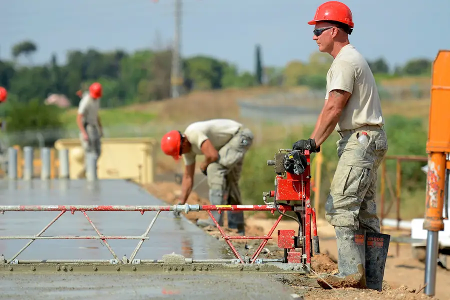Worker screeding wet concrete over reinforcing mesh